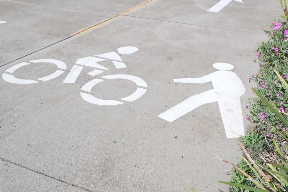 Close-up of white pedestrian and bike symbols painted on concrete path.